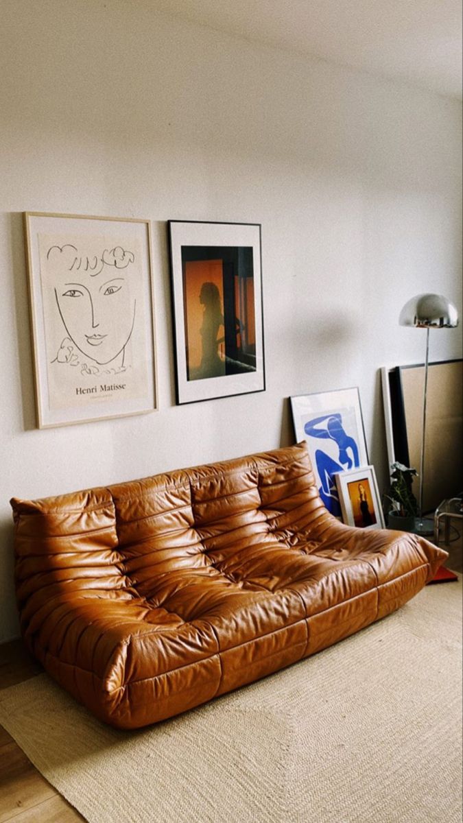 a brown leather couch sitting in a living room next to two pictures on the wall