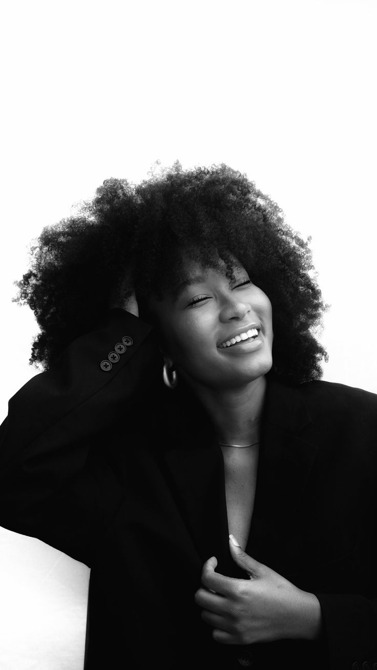 a woman with an afro is smiling and holding her hair up to her face while wearing a black blazer