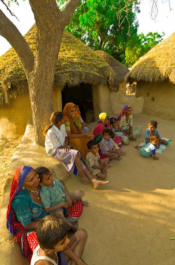 a group of people sitting on the side of a dirt road next to a tree