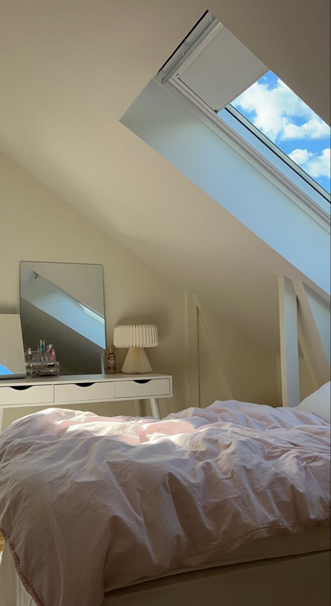 an attic bedroom with skylights and a bed in the foreground is seen from across the room