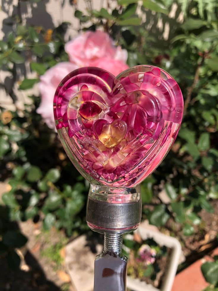 a heart shaped glass object sitting on top of a metal stand in front of flowers