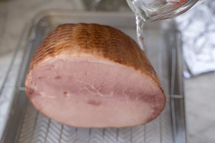 a ham is being cooked in the oven with a bottle of water next to it