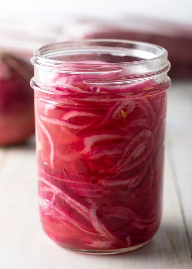 a jar filled with red onions sitting on top of a wooden table next to an apple