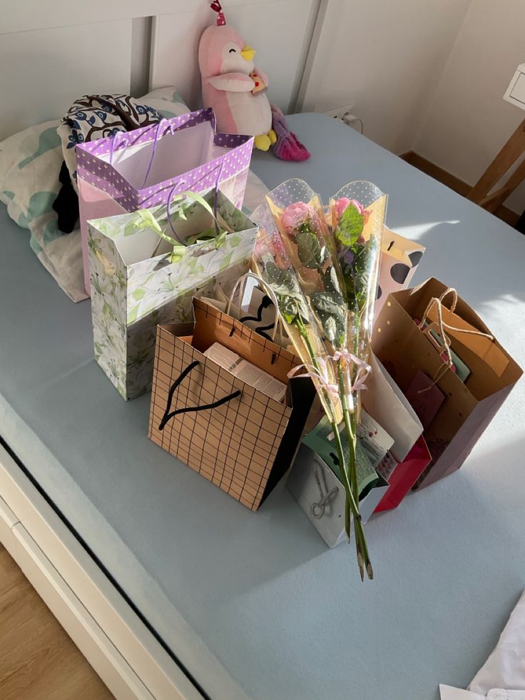 several boxes and flowers on a bed with a stuffed animal in the corner behind them