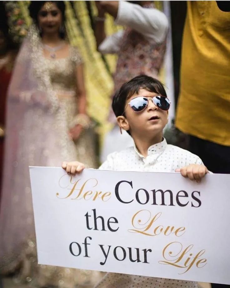 a young boy holding a sign that says here comes the love of your life