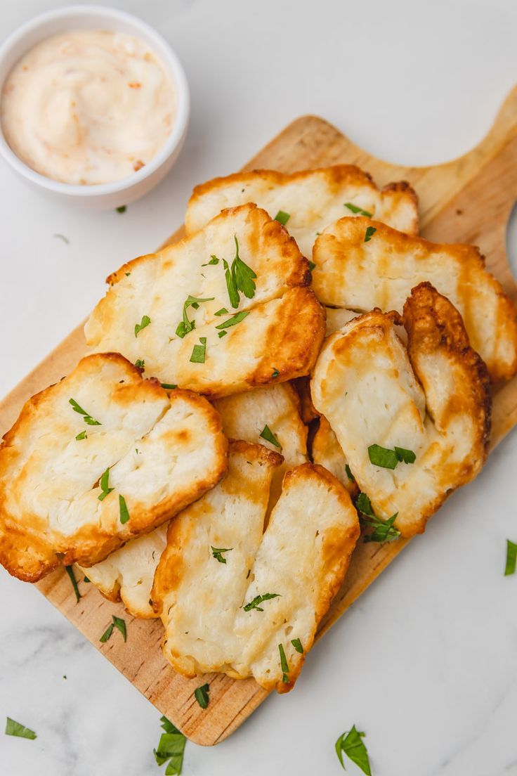 some food is laying on a cutting board next to a small bowl of dip sauce