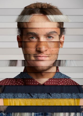 a man with white hair and blue eyes is looking at the camera through some blinds