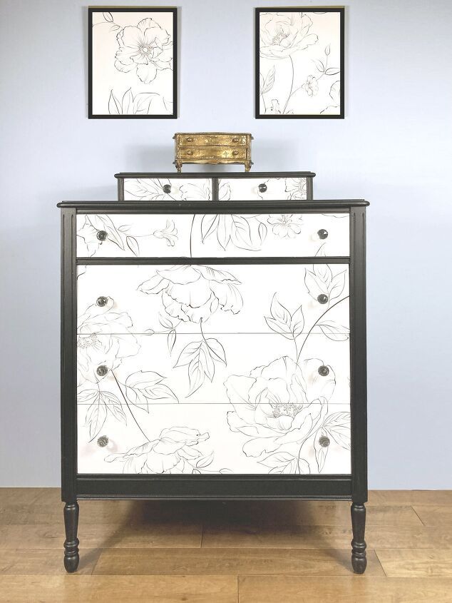 a black and white dresser with flowers painted on the front, two framed pictures above it