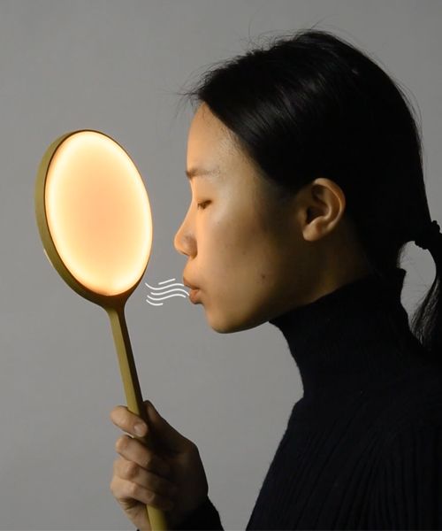 a woman holding a light up to her face and blowing it's nose into the air