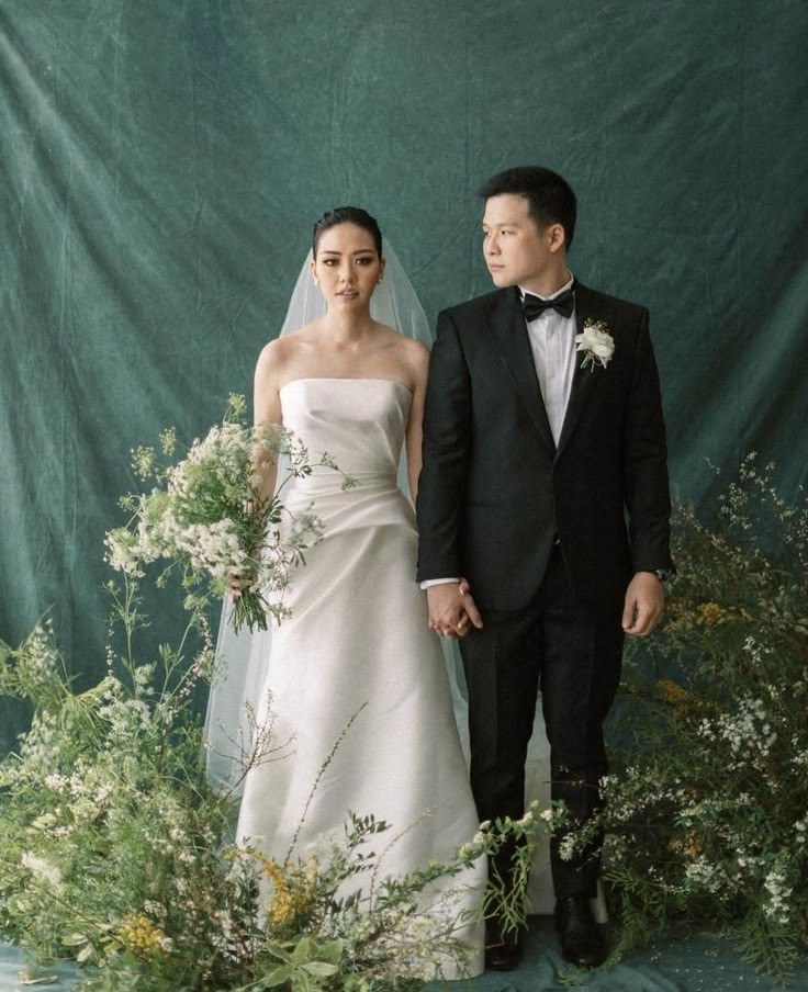 a man and woman standing next to each other in front of flowers, grass and cloth