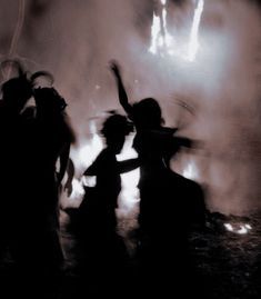 silhouettes of people dancing in front of a firework display at night with bright lights