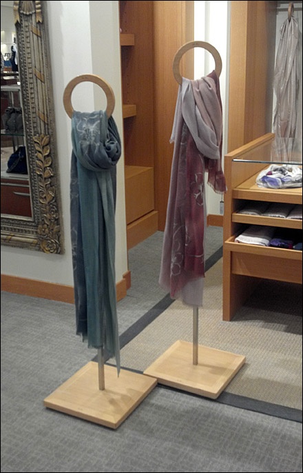 two wooden clothes racks with scarves and scarfs on them in front of a mirror