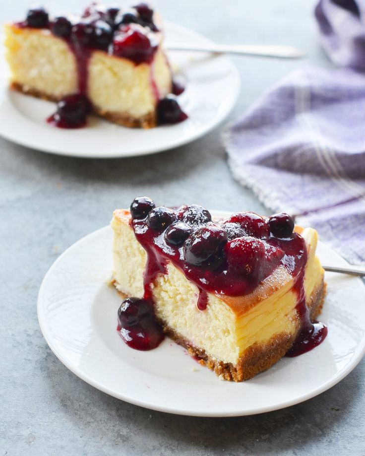 two slices of cheesecake with blueberry sauce on white plates