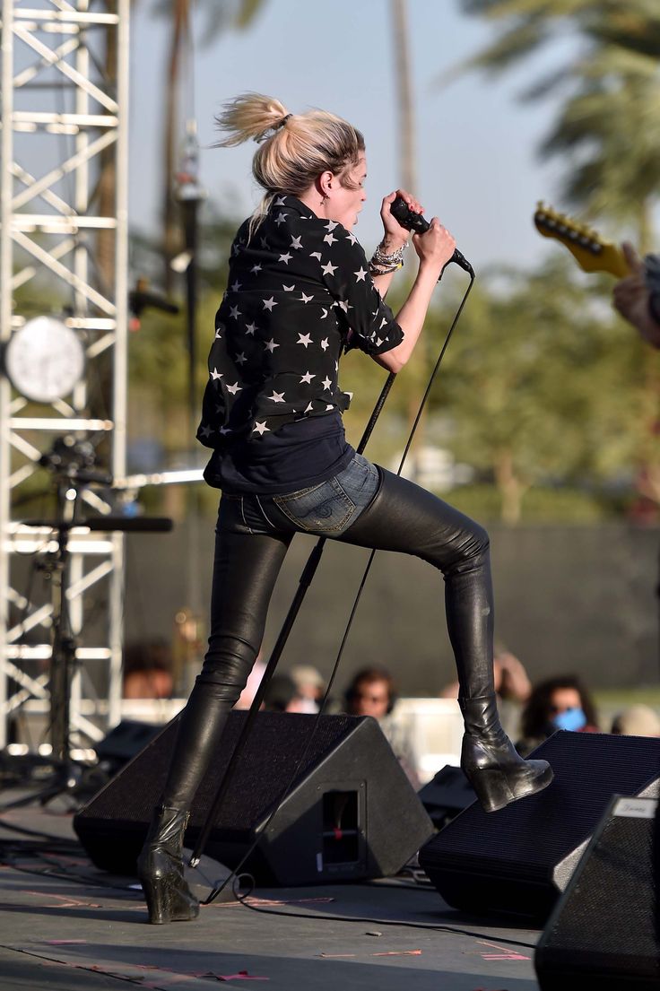 a woman on stage with a guitar and microphone in her hand, performing at an outdoor concert