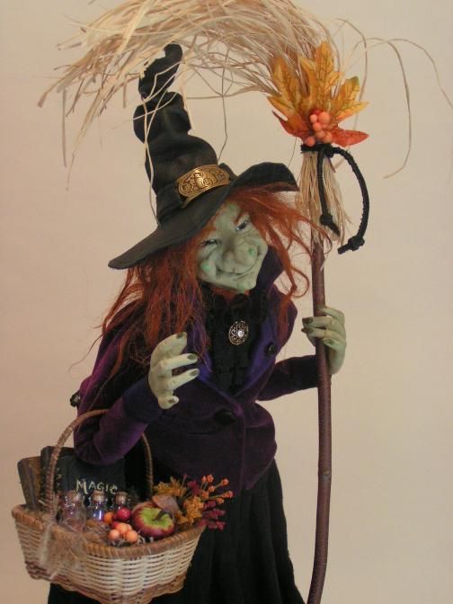 a doll dressed as a witch holding a broom and basket with an orange flower in it