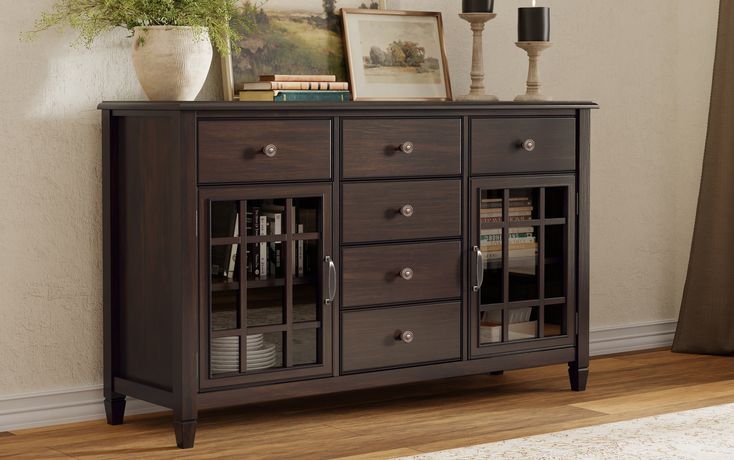 a sideboard with glass doors and drawers in a room next to a lamp on the wall