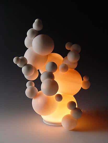 a white vase filled with lots of balls on top of a table next to a lamp