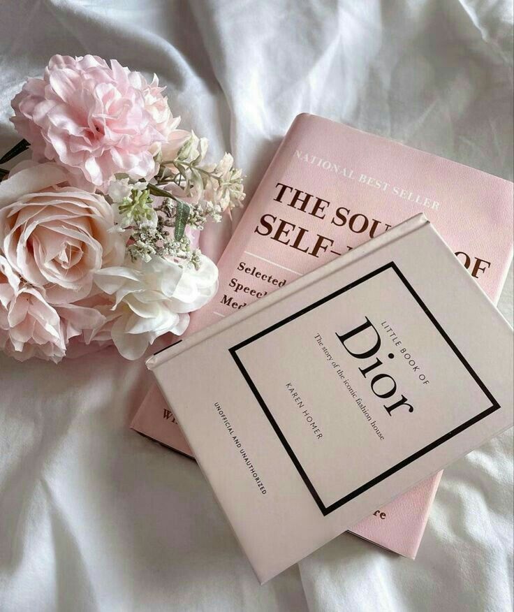 two pink books sitting on top of a bed next to a bouquet of white and pink flowers