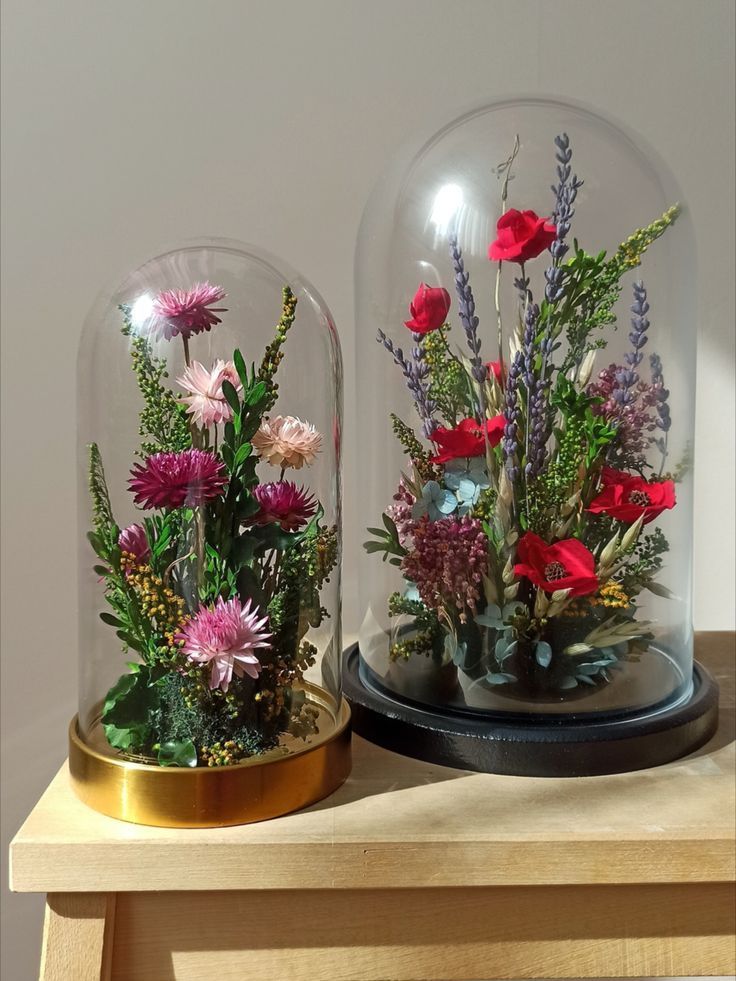 two glass domes filled with flowers on top of a wooden table next to each other