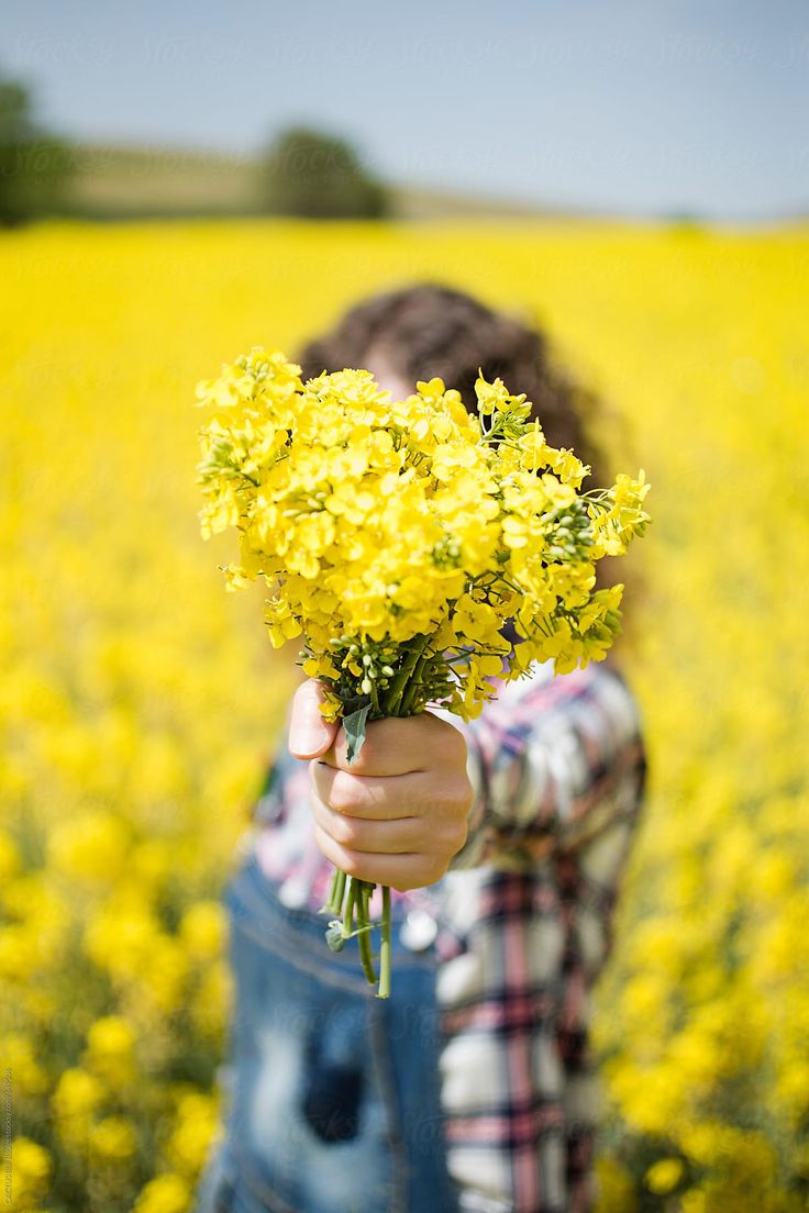 a person holding flowers in front of a yellow field