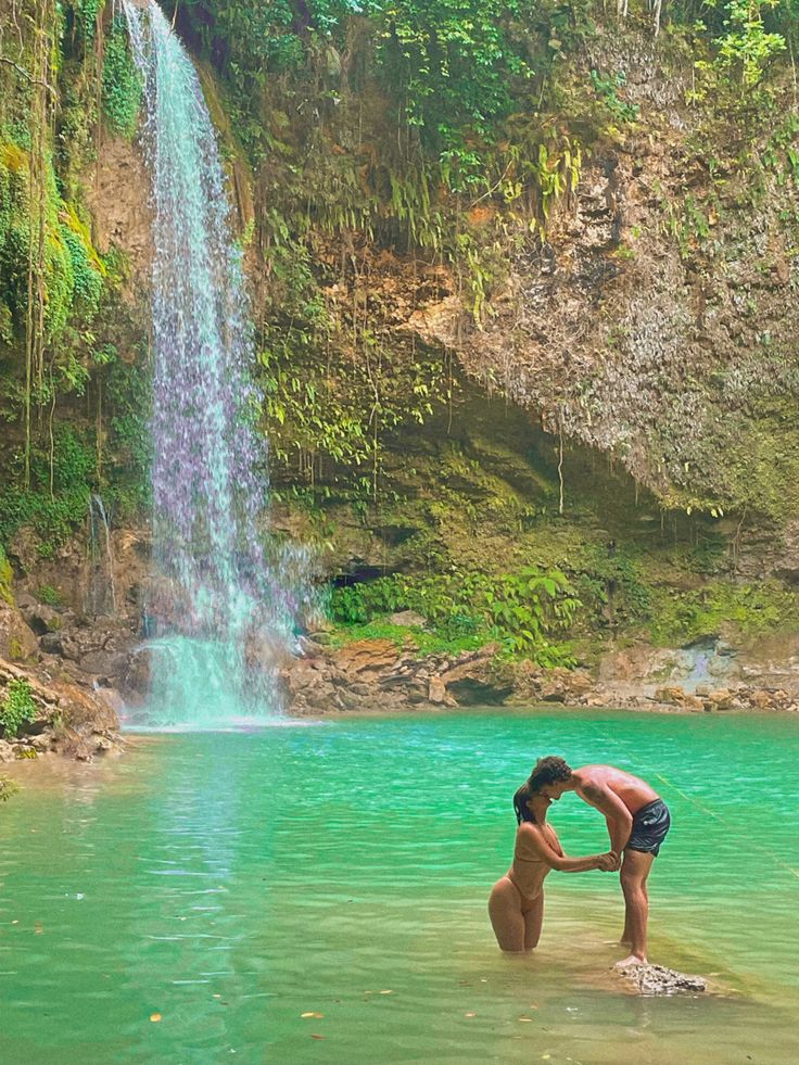 a man standing in the water next to a waterfall