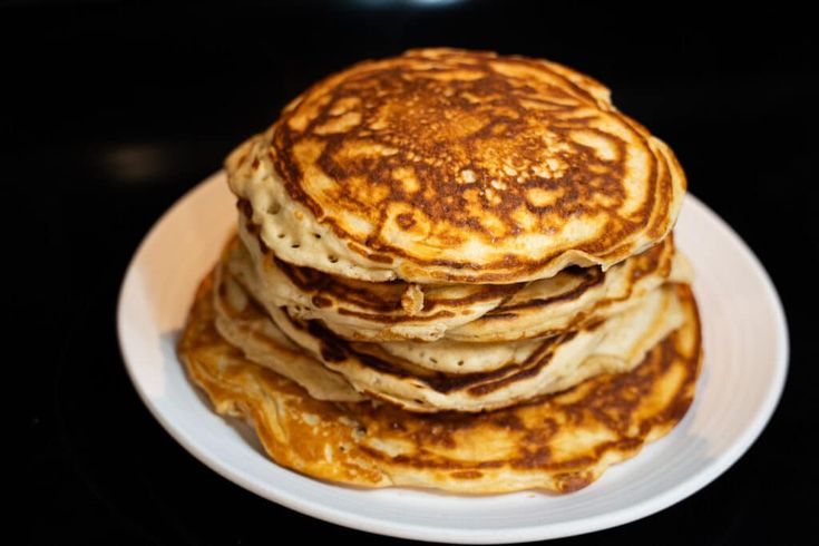 a stack of pancakes sitting on top of a white plate next to a black counter