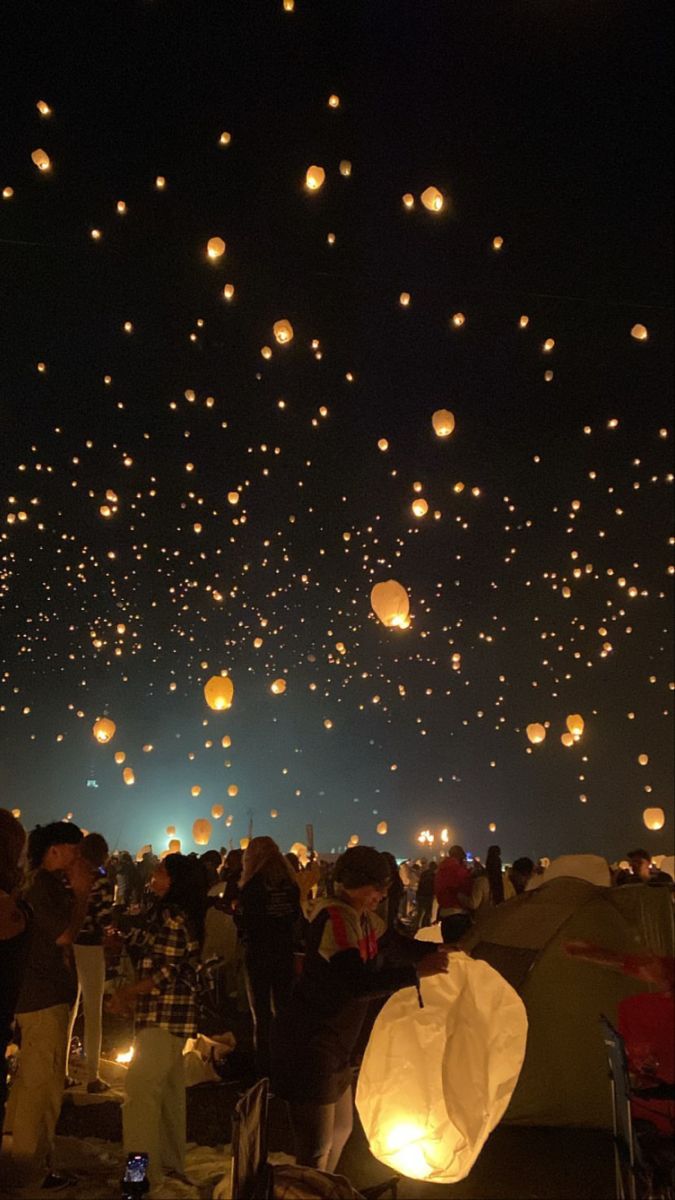 the sky is filled with many lanterns floating in the night sky and people looking at them