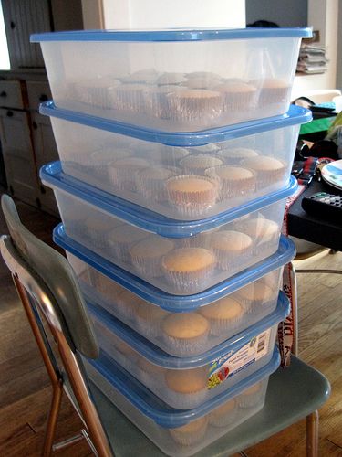 a stack of plastic containers filled with cupcakes on top of a wooden table