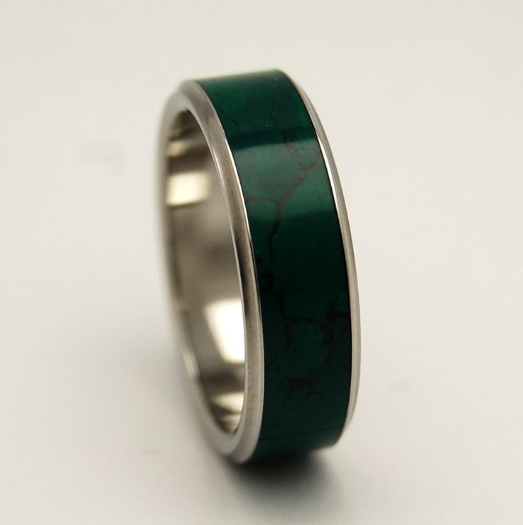 a wedding ring with green and silver inlays on the inside, sitting on a white surface