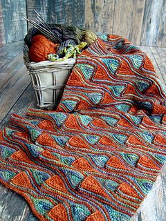 a crocheted blanket sitting on top of a wooden floor next to a basket filled with yarn