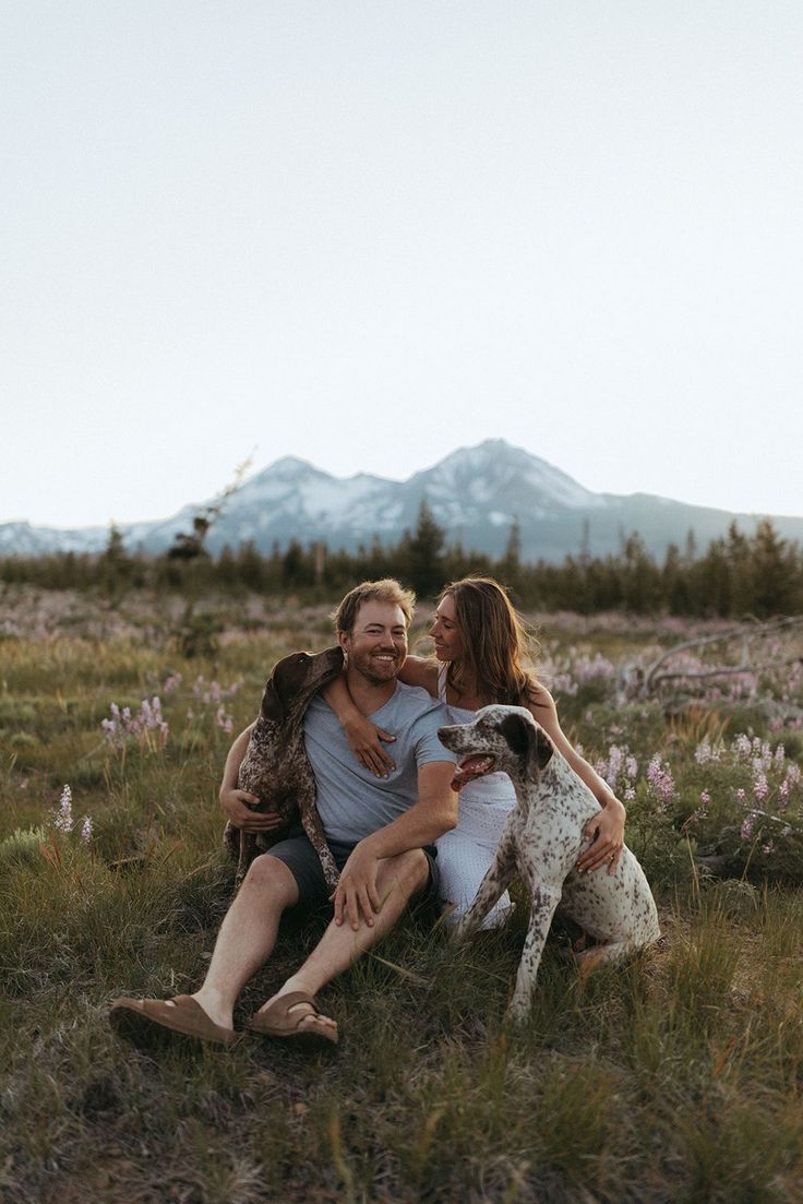 a man and woman sitting in the grass with a dog