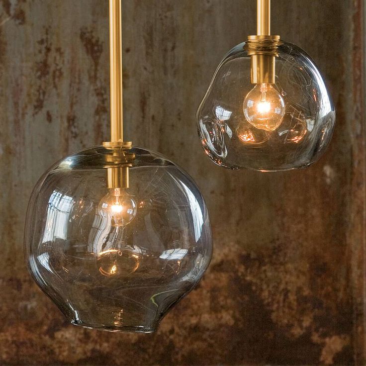 two clear glass globe lights hanging from a ceiling fixture with gold colored metal fittings