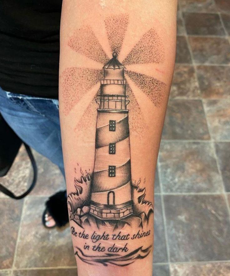 a person with a tattoo on their arm that has a lighthouse in the middle and words above it