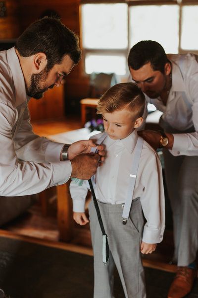 a man helping a little boy put on his bow tie in front of another man