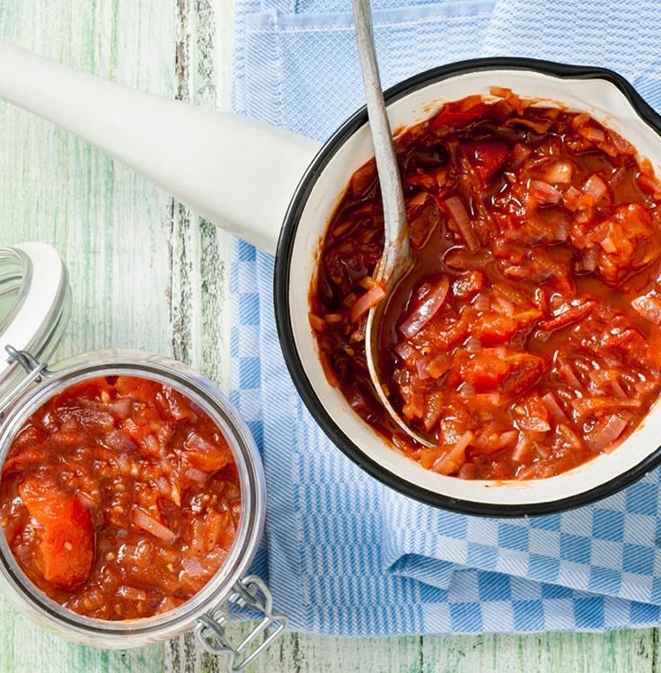 a bowl filled with chili next to two jars of sauce on a blue and green towel