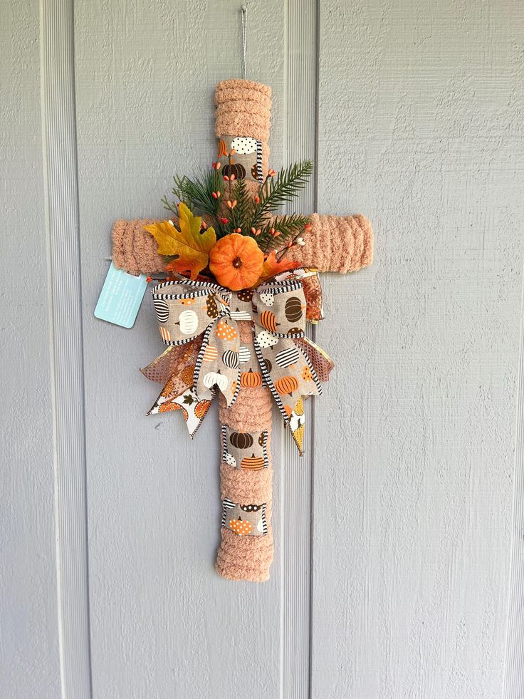 a crocheted cross hanging on the side of a door with fall leaves and pumpkins