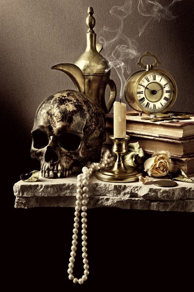 a table topped with a skull and a clock next to a candle on top of a table