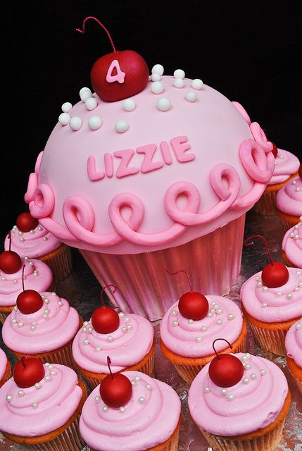 cupcakes with pink frosting and cherries are arranged around a heart shaped cake