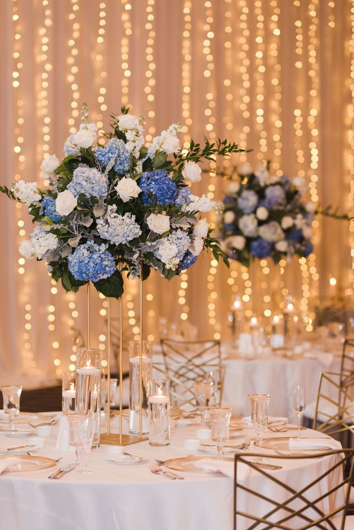 the table is set with blue and white flowers in tall vases on each side