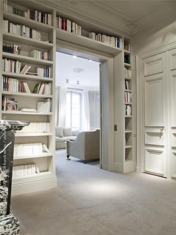 a living room filled with lots of white furniture and bookshelves next to a doorway