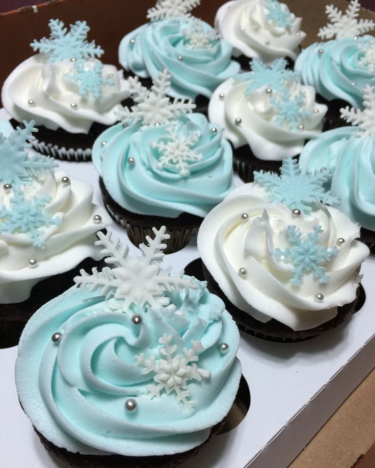 cupcakes with frosting and snowflakes on them are in a box