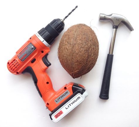 an electric screwdriver, hammer and coconut on a white surface with other tools