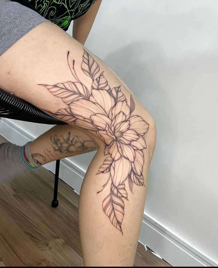 a woman sitting on a chair with her legs crossed and flowers tattooed on the leg