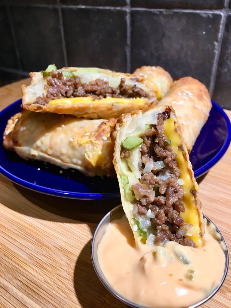 two burritos on a blue plate with dip in the middle next to it