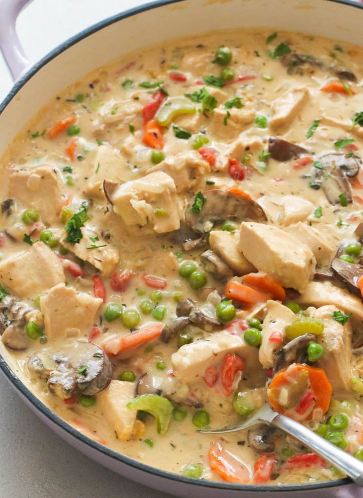 a pot filled with chicken and vegetables on top of a table next to a spoon