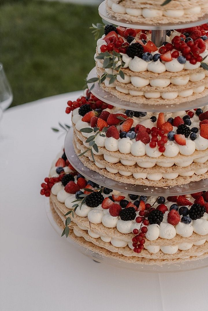 a three tiered cake with berries and cream on top sits on a white table