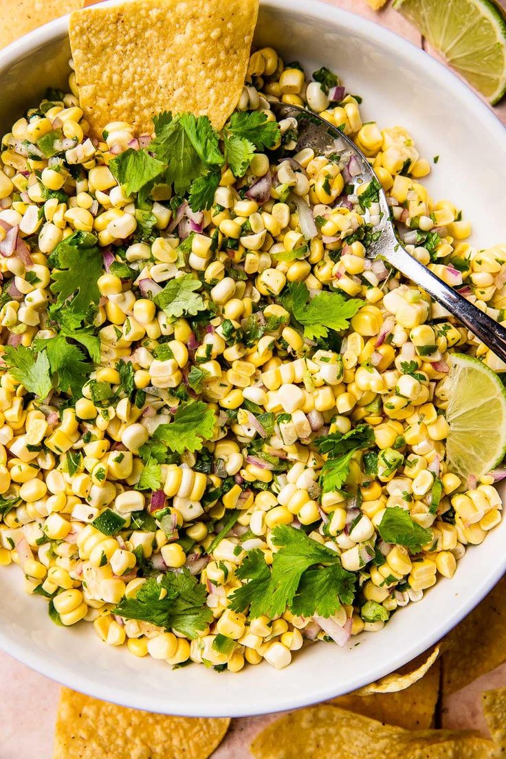 corn salad with cilantro and lime in a white bowl surrounded by tortilla chips