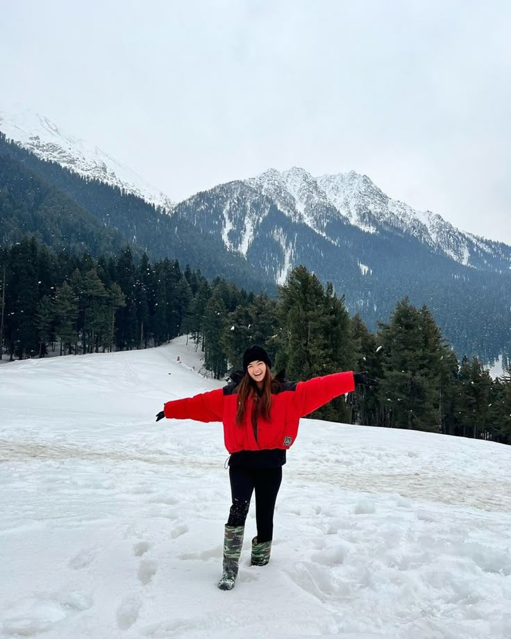 a woman standing in the snow with her arms spread out and mountains in the background