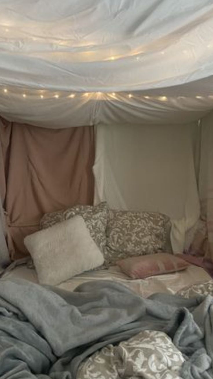 a bed covered in blankets and pillows under a canopy with fairy lights on the ceiling