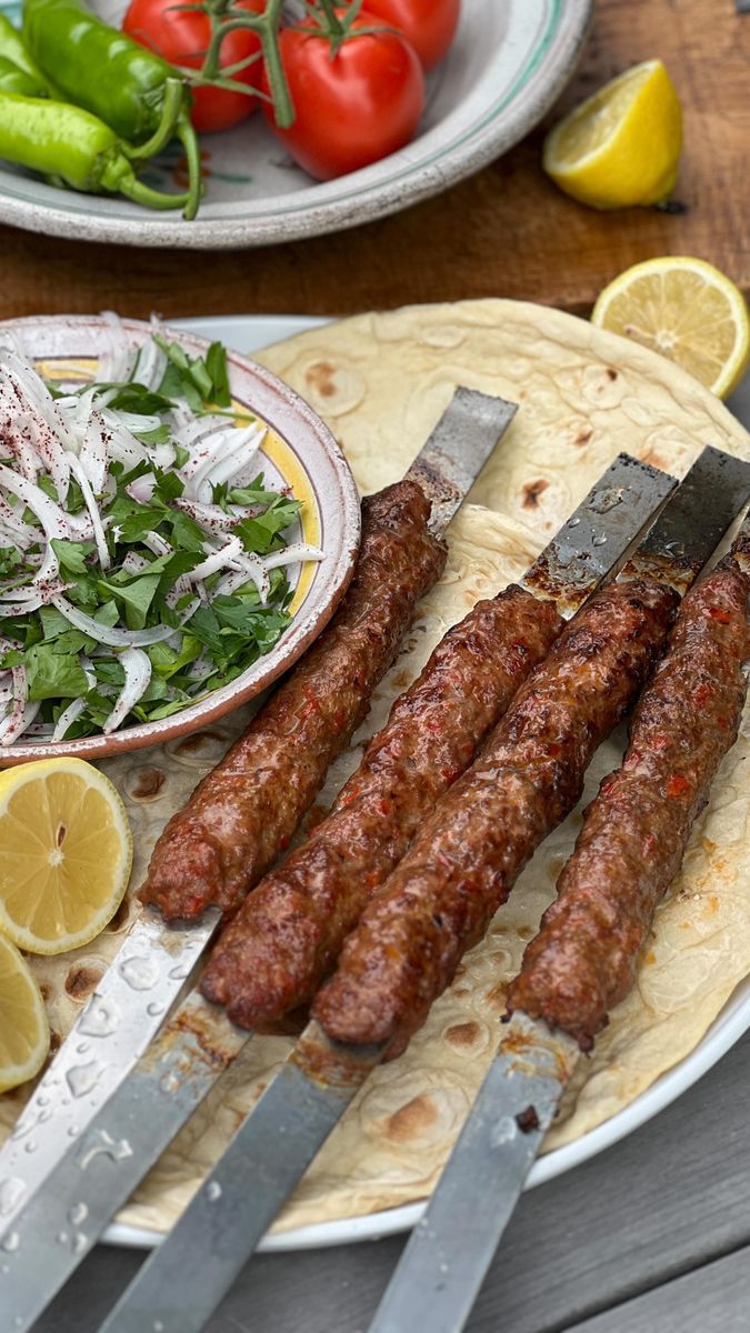 there are several sausages on the plate with lemon wedges next to some salad